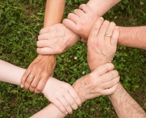 Arme von 6 Menschen, die sich jeweils auf das Handgelenk greifen und so einen Kreis bilden